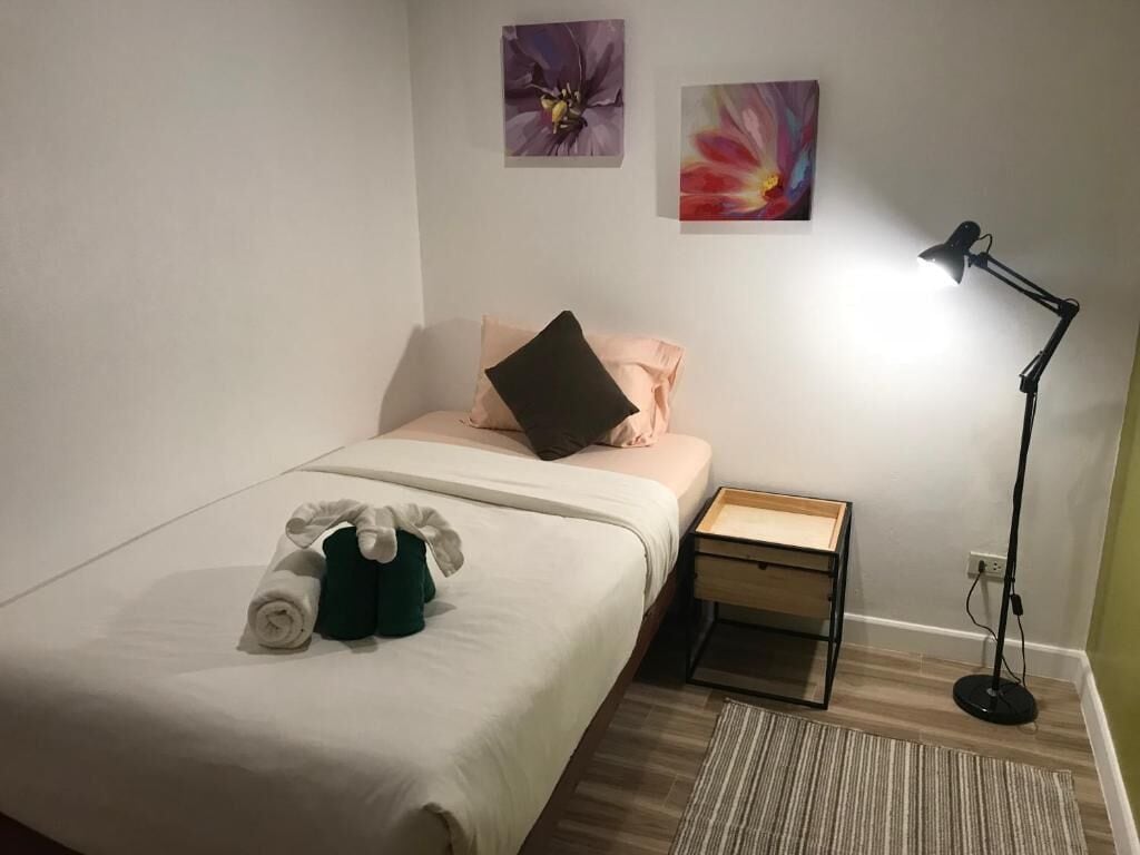 En snyggt bäddad säng med en kudde, ett sängbord med en lampa och två tavlor på väggen.