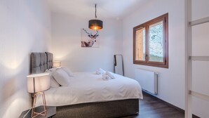 Une chambre à coucher avec un lit, des lampes de chevet, un tableau accroché au mur, une fenêtre donnant sur des arbres couverts de neige et un radiateur.