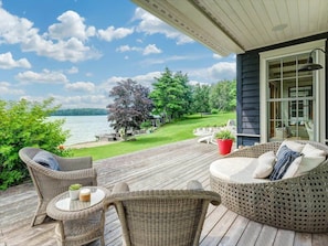 A wooden deck with wicker furniture, a glass table, and a view of a lake and trees. - Exclusive Waterfront Getaway with Beach & Bunkie (Portland)