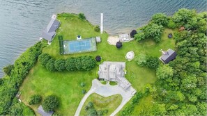 Surrounded by lush greenery and a body of water, this property offers a tennis court and panoramic views from its main building.