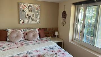 A bedroom with a bed, pillows, a bedside table, a lamp, a window, and a wall decoration.