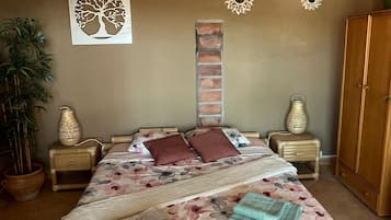 A bedroom with a bed, a hanging light fixture, a wall-mounted decorative piece, and a potted plant.