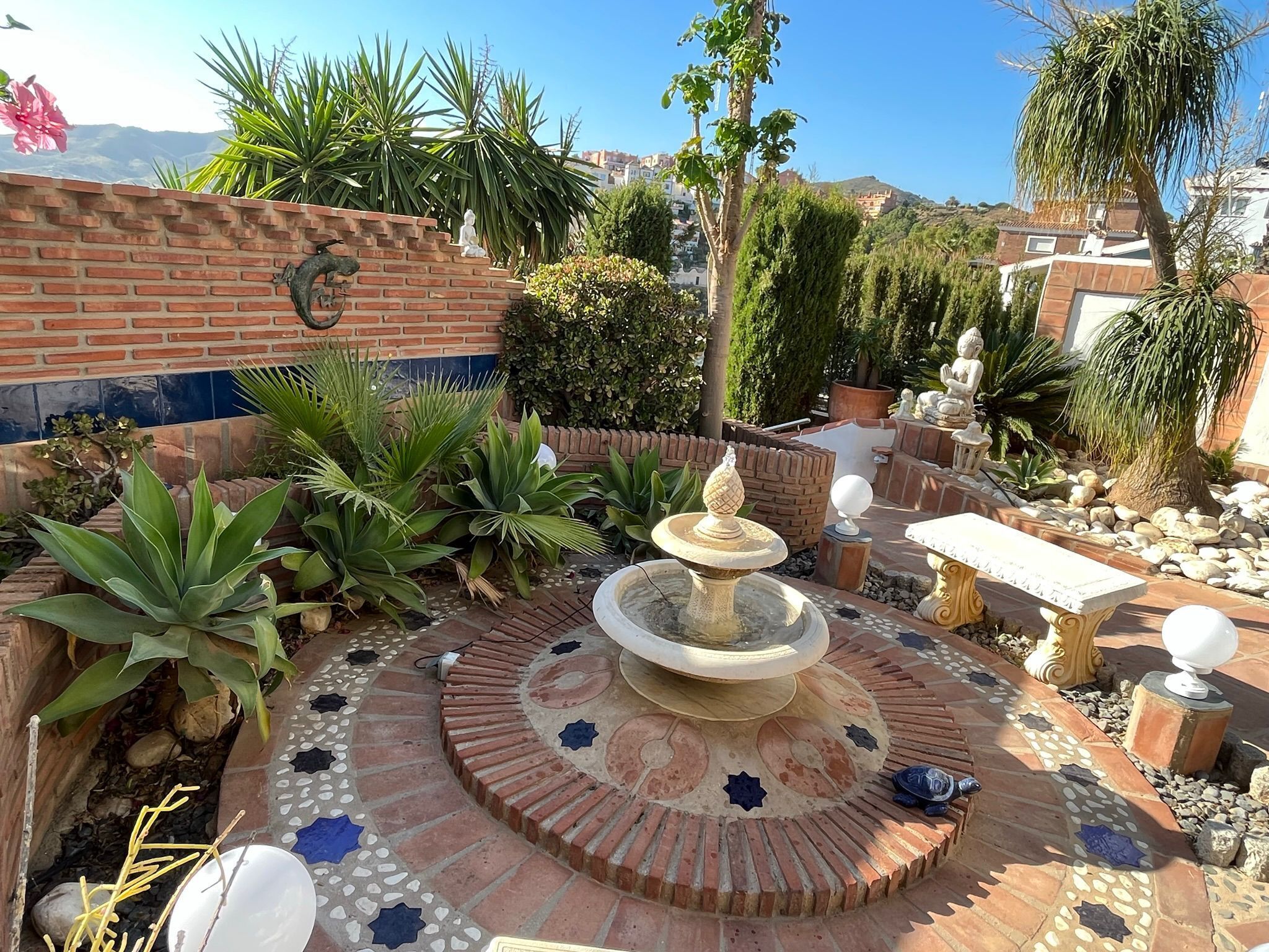 A courtyard with a fountain, potted plants, and a brick wall.