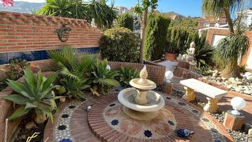 Un patio con una fuente, plantas en macetas y un muro de ladrillo.