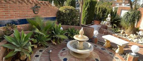 A courtyard with a fountain, potted plants, and a brick wall.