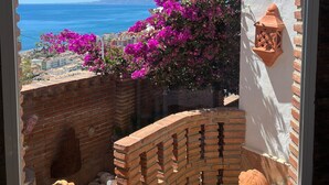 Een balkon met uitzicht op zee, een bakstenen muur en een wit gebouw met een terracotta pot.