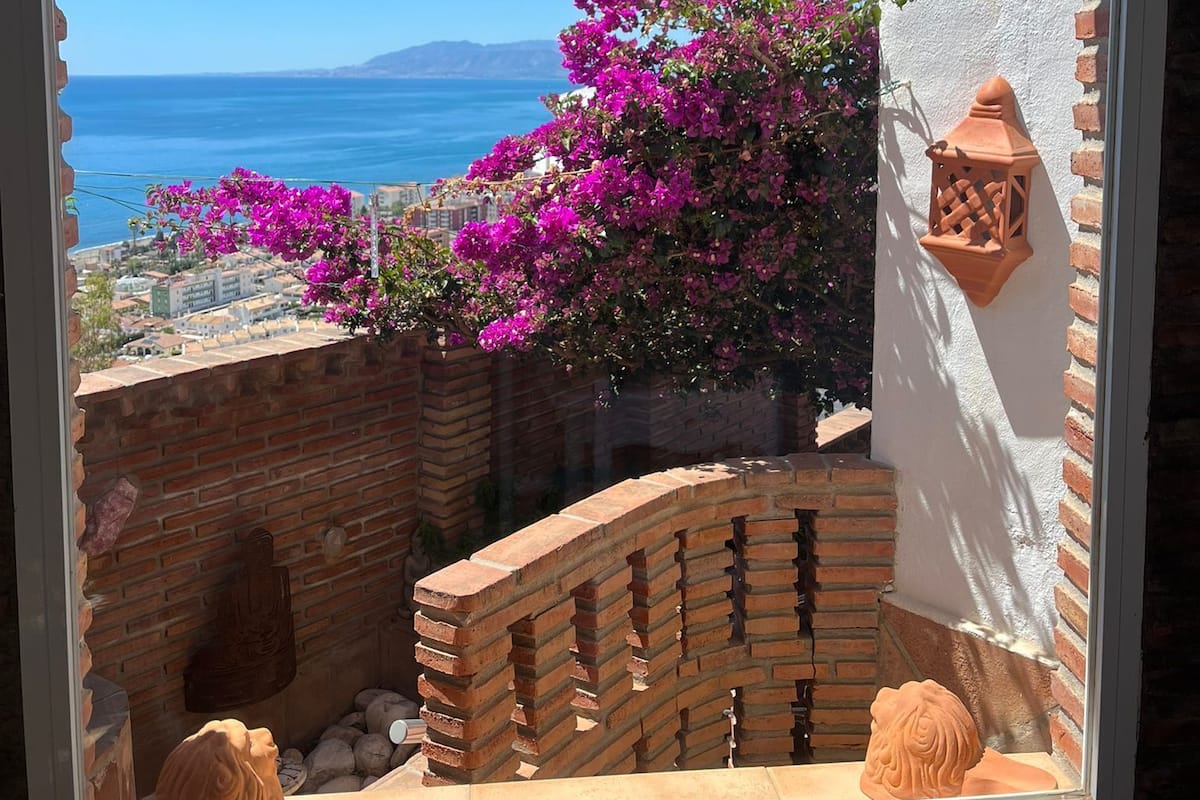 Un balcón con vista al mar, un muro de ladrillo y un edificio blanco con una maceta de terracota.