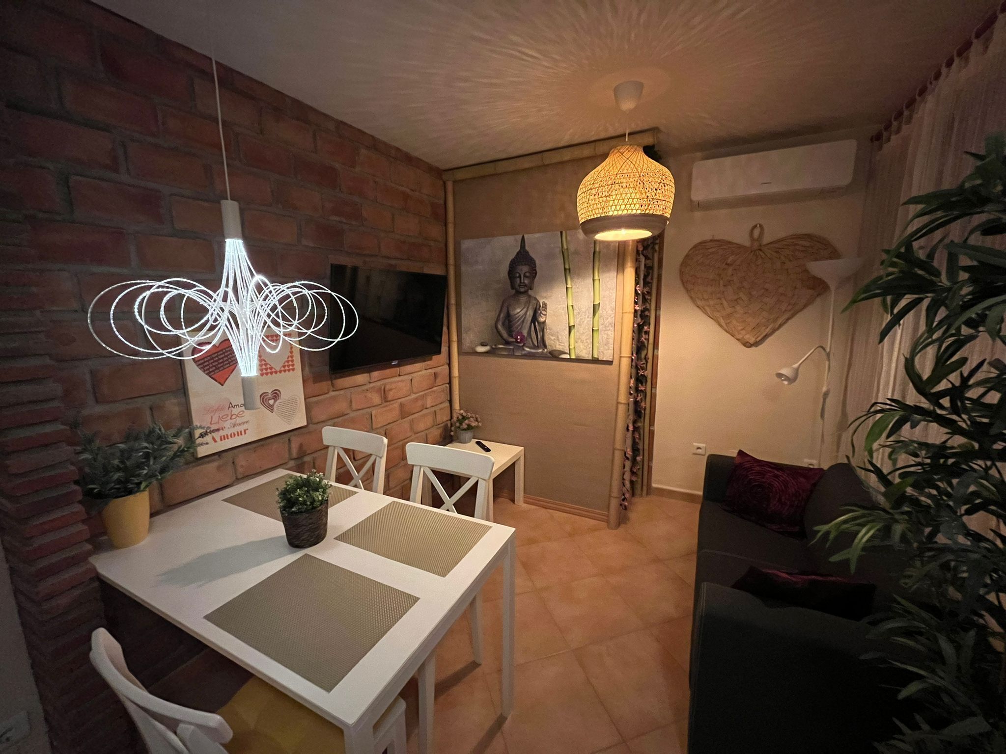Un comedor acogedor con pared de ladrillo, un televisor sobre la mesa y una lámpara colgante.