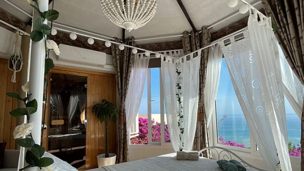 Een slaapkamer met een hemelbed, een hangende kroonluchter en uitzicht op zee.