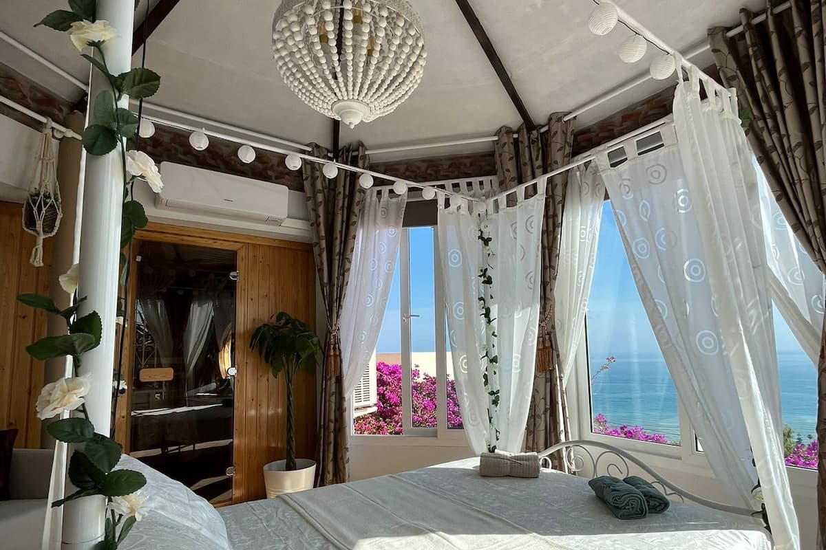 Un dormitorio con cama con dosel, un candelabro colgante y vista al mar.