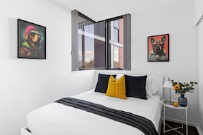 Ein modernes Schlafzimmer mit einem großen Bett, einem Fenster mit freier Aussicht und zwei gerahmten Kunstwerken an den Wänden.