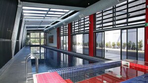 En inomhuspool med stora fönster som ger fri sikt utåt, ett kaklat golv och en metallstege.
