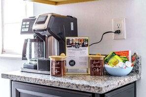 A coffee station with a coffee machine, two jars labeled "Local Bucks Coffee," a bowl with coffee packets, and a sign promoting local coffee shops.