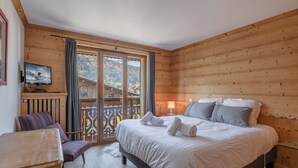 Una habitación de madera con una cama, una silla, un televisor y un balcón con vistas a un pueblo.