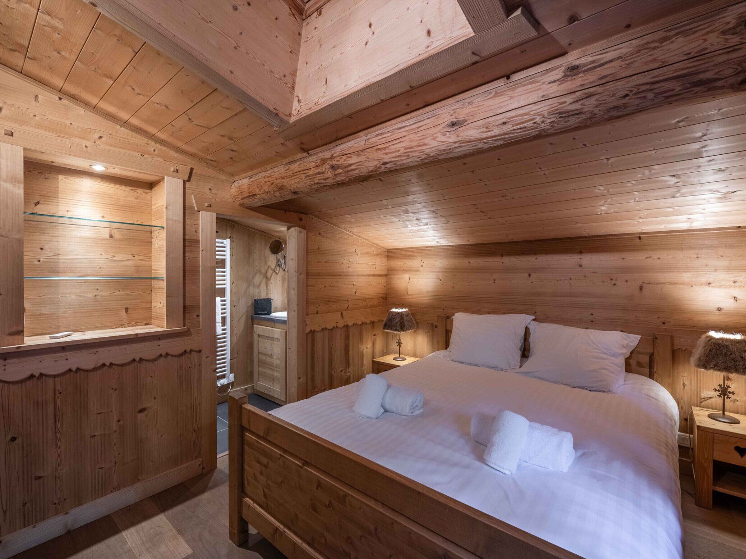 A wooden cabin bedroom with a bed, nightstands, a lamp, and a window.