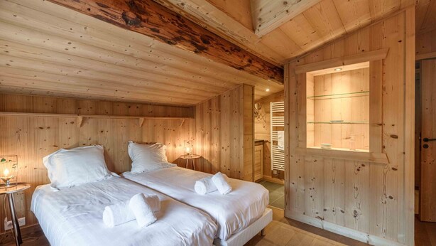 Una habitación de madera con dos camas, una mesita y un ventanal grande.