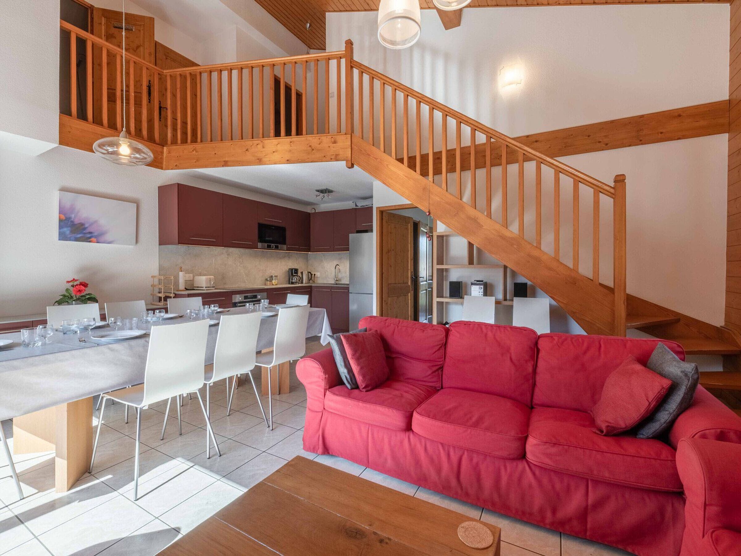 Een ruime woonkamer met een houten trap, een eettafel voor vier personen en een rode bank.