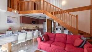 Amplia sala de estar con escalera de madera, mesa de comedor para cuatro comensales y un sofá rojo.