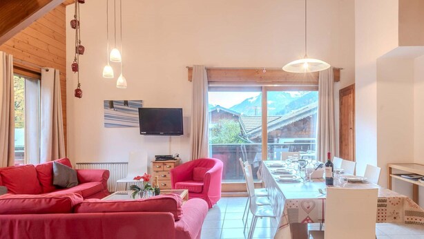 Una sala de estar moderna con un sofá rojo, una mesa de comedor preparada para cuatro personas y un televisor montado en la pared.