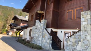 Una cabaña de madera con escaleras de piedra y varias ventanas, rodeada por un paisaje montañoso.