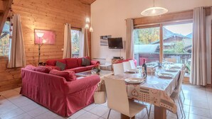 Una habitación acogedora con un sofá rojo, una mesa de comedor preparada para dos personas y un televisor montado en la pared.