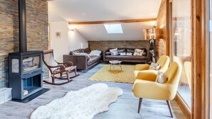 Una sala de estar acogedora con chimenea, sofás de cuero, un sillón mecededor y un ventanal grande.