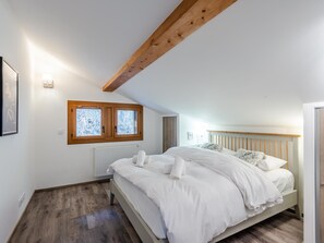 Un dormitorio con viga de techo de madera, cama con ropa de cama blanca, radiador y ventana con vidrio esmerilado.