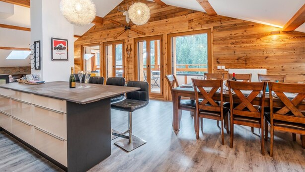 Una cocina amplia con vigas de madera, una isla central y un comedor con sillas de madera.