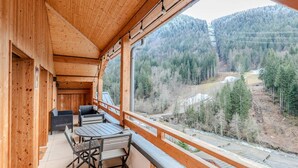 Un balcón de madera con una mesa y sillas, con vistas a un valle boscoso.