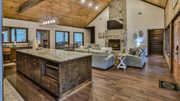 A spacious living area with a large island, stone fireplace, and wooden ceiling beams. - Sweet Magnolia~Sleeps 10~Game Area~2 Masters (Broken Bow)