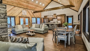 A spacious living area with a high wooden ceiling, a stone fireplace, and a dining area with a wooden table and chairs. - Sweet Magnolia~Sleeps 10~Game Area~2 Masters (Broken Bow)