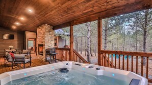 A hot tub on a wooden deck with a stone fireplace and a TV mounted on the wall. - Sweet Magnolia~Sleeps 10~Game Area~2 Masters (Broken Bow)