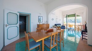 A dining area with a wooden table and chairs, a kitchen in the background, and a view through an archway to an outdoor patio. - Villa Cavalluccio Marino (Campania)