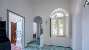 A hallway with a tiled floor, a door leading to another room, and a window with a view of trees. - Villa Cavalluccio Marino (Campania)