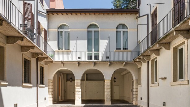 A courtyard with a building featuring a balcony, arched doorways, and stone pillars. - Book Lovers@ArenaTheatre (Verona)