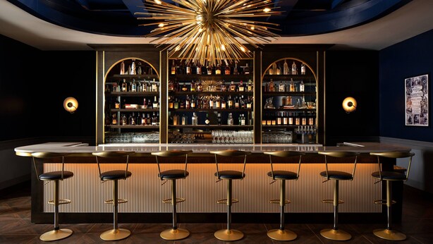 A bar area with a central light fixture, multiple shelves of bottles, and bar stools. - Trilith Guesthouse, Fayetteville, GA, A Tribute Portfolio (Fayetteville)