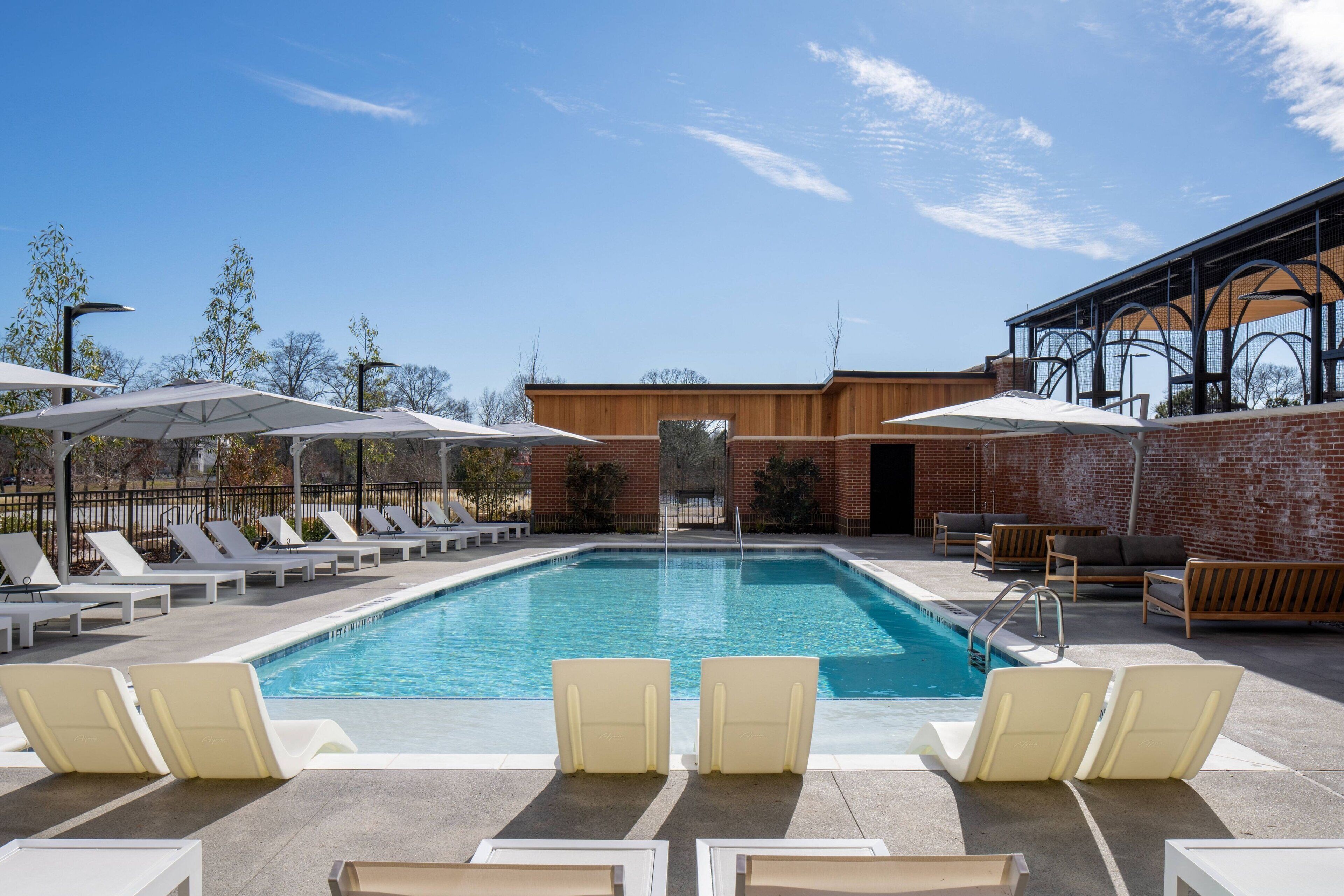 A swimming pool with lounge chairs and umbrellas, surrounded by a brick wall and trees.