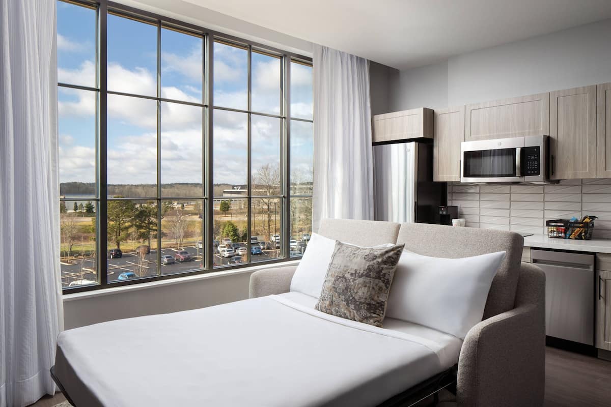 A modern room with a large window, a sofa, a microwave, and a kitchen area.