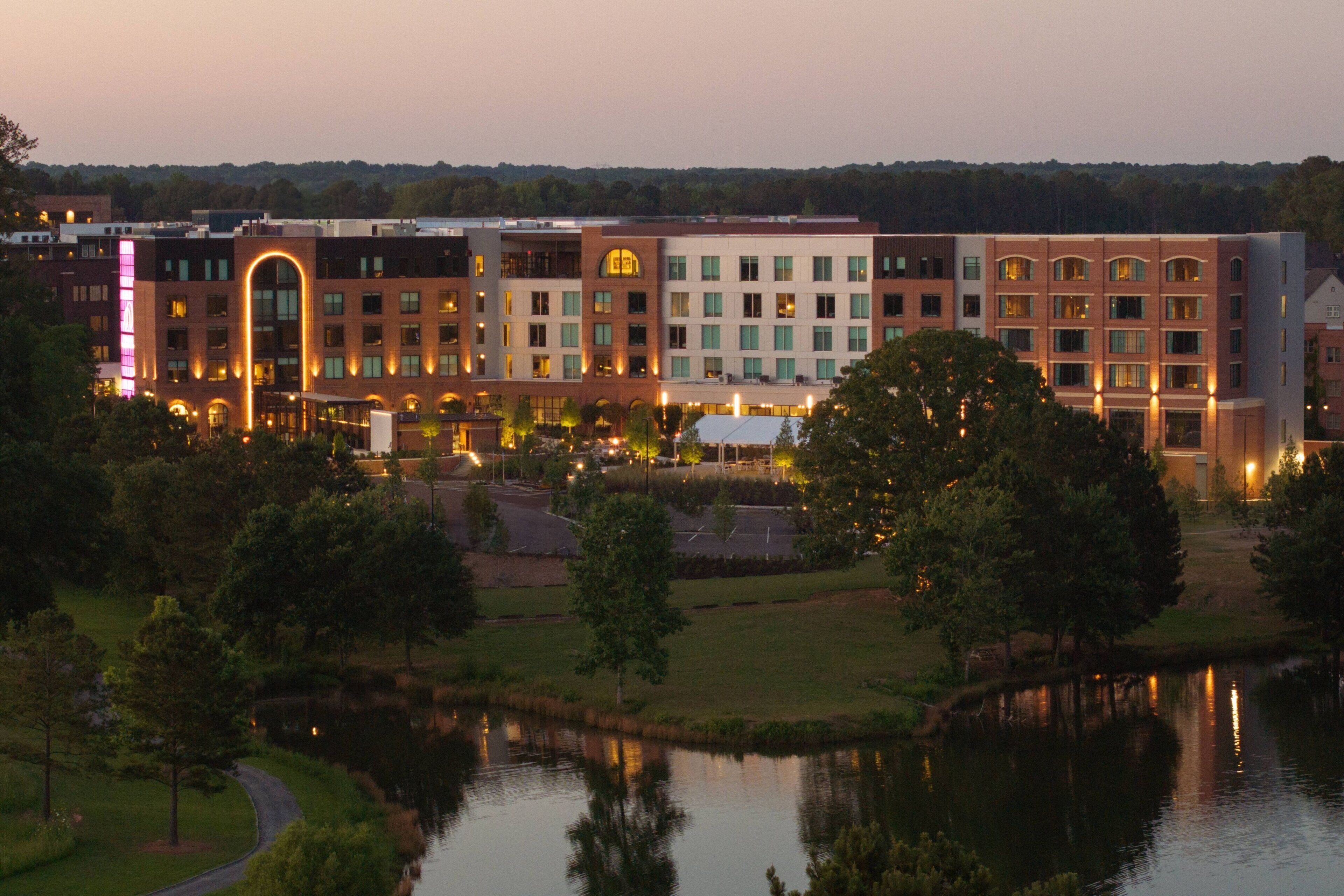 A multi-story hotel with a central courtyard, a pond, and a parking area.