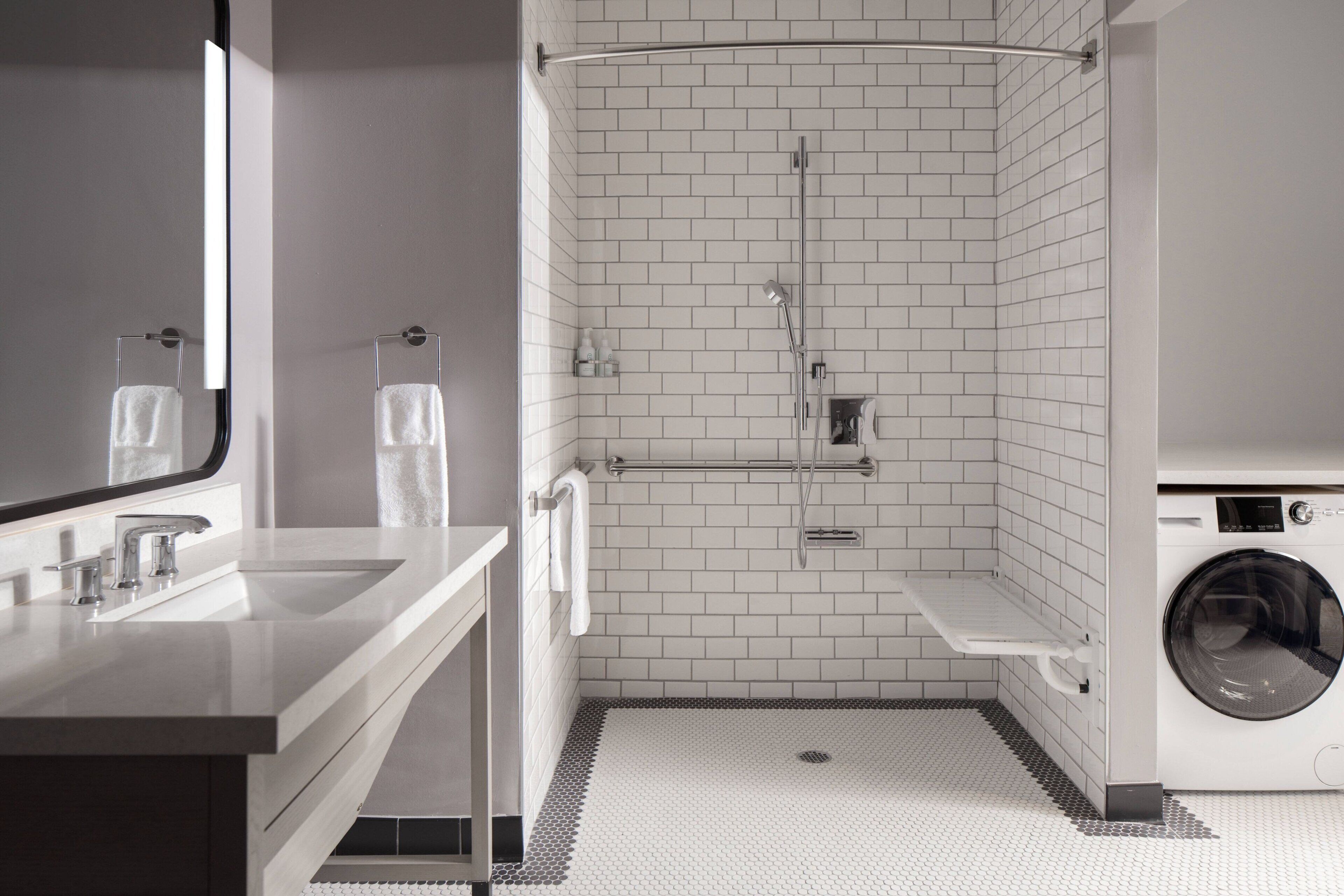 A modern bathroom with a sink, mirror, shower, and washing machine.