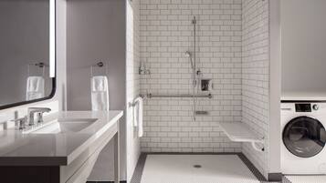 A modern bathroom with a sink, mirror, shower, and washing machine.