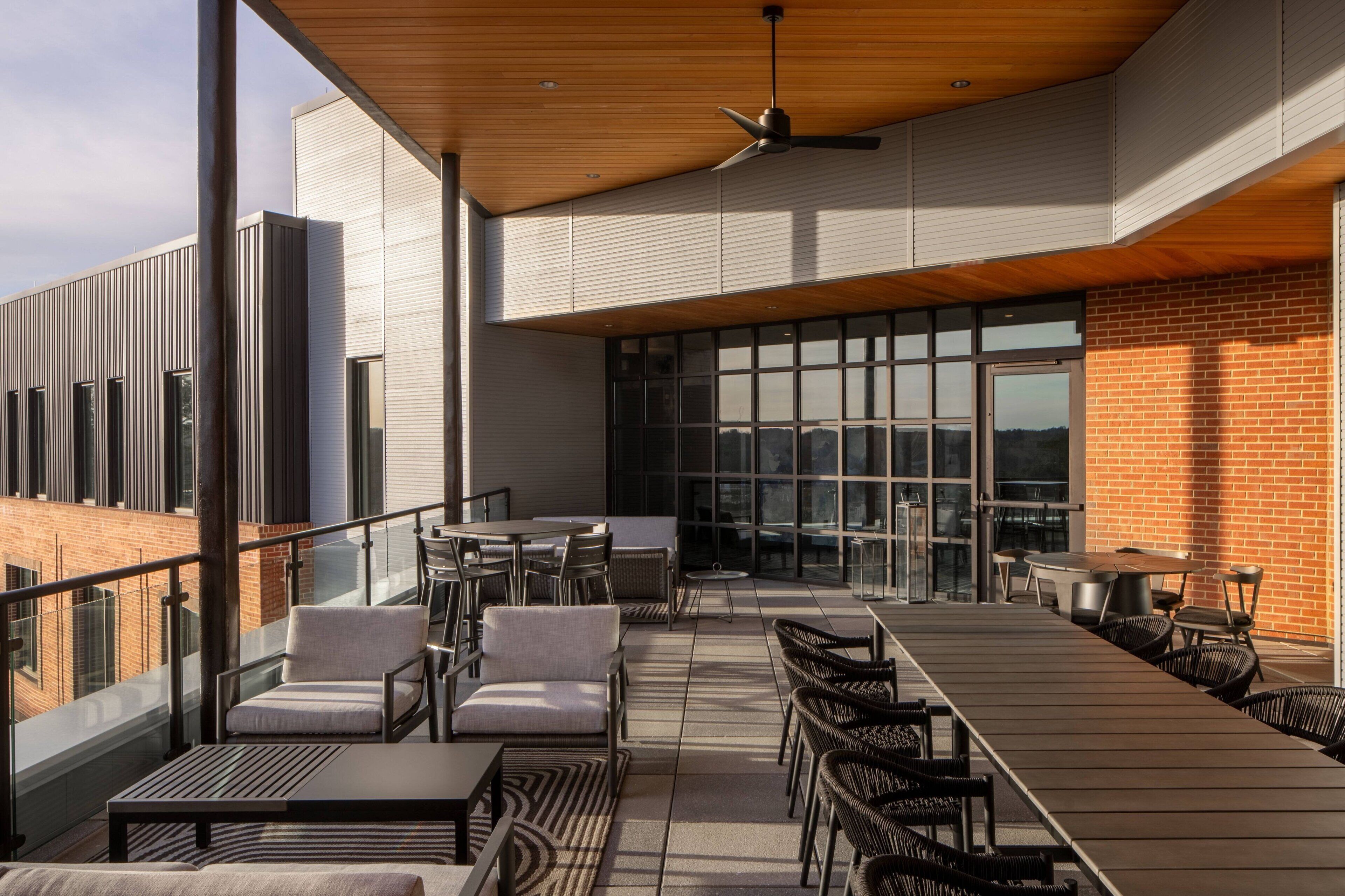 A rooftop terrace with outdoor seating, a fan, and large windows.