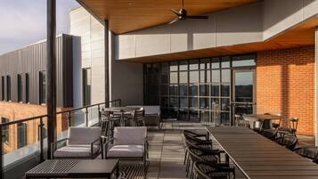 A rooftop terrace with outdoor seating, a fan, and large windows.