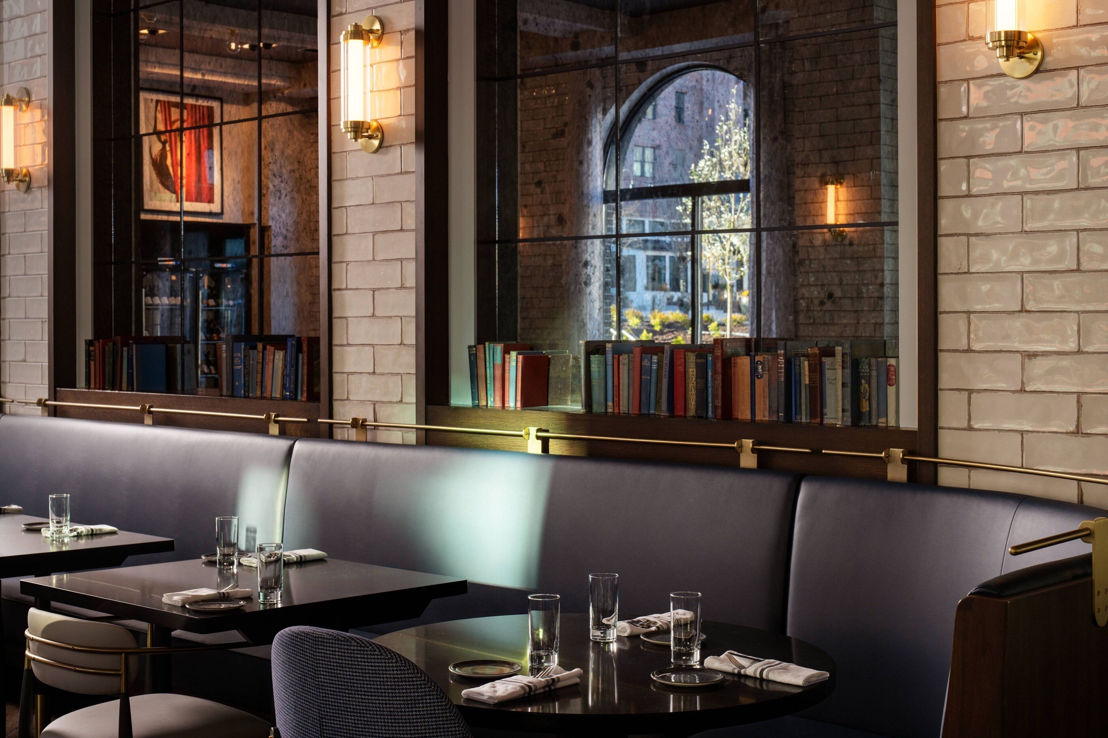 A restaurant with a brick wall, bookshelves, and a view through a large window.