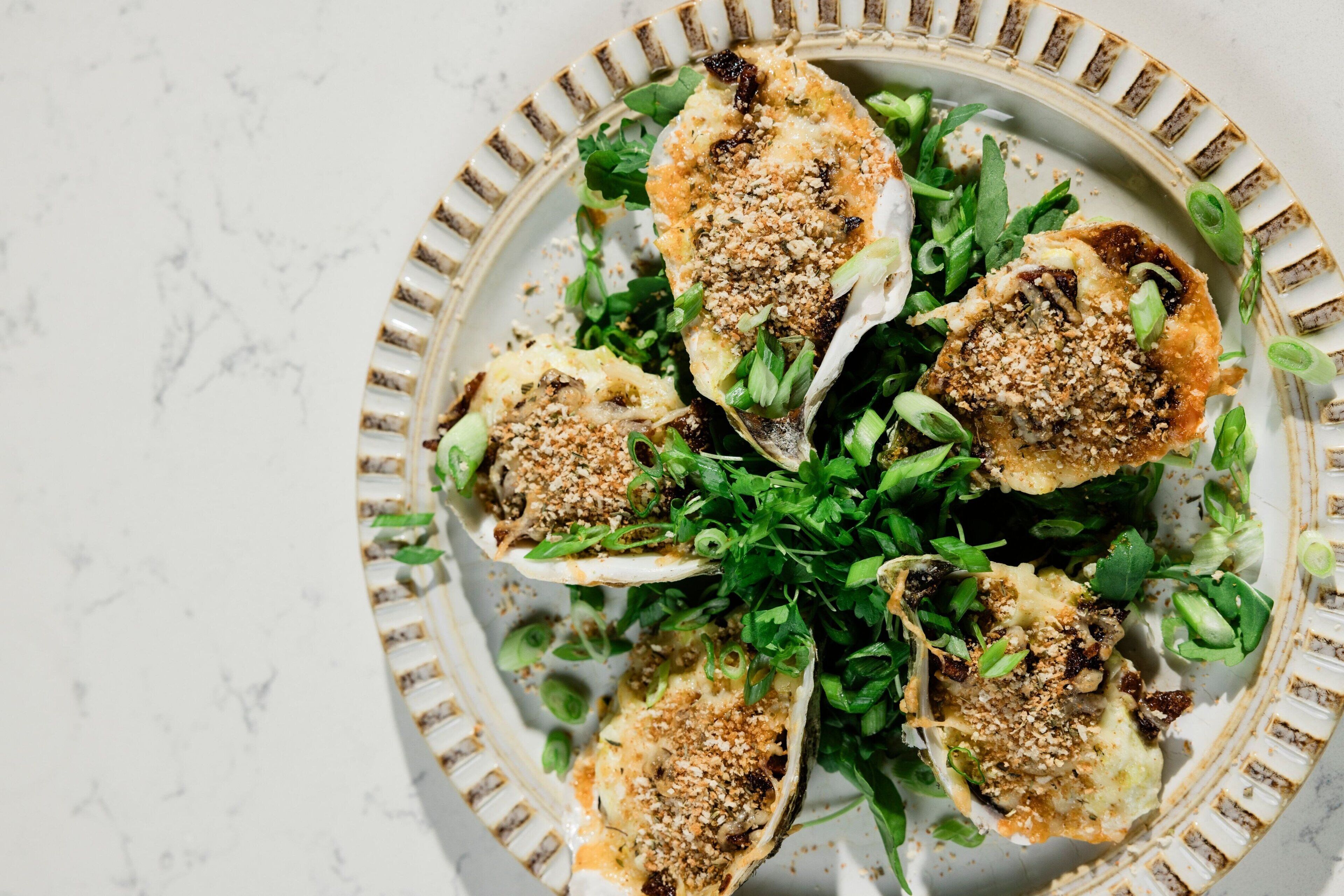 A plate with food items, including what appears to be stuffed mushrooms and greens, on a white marble surface.