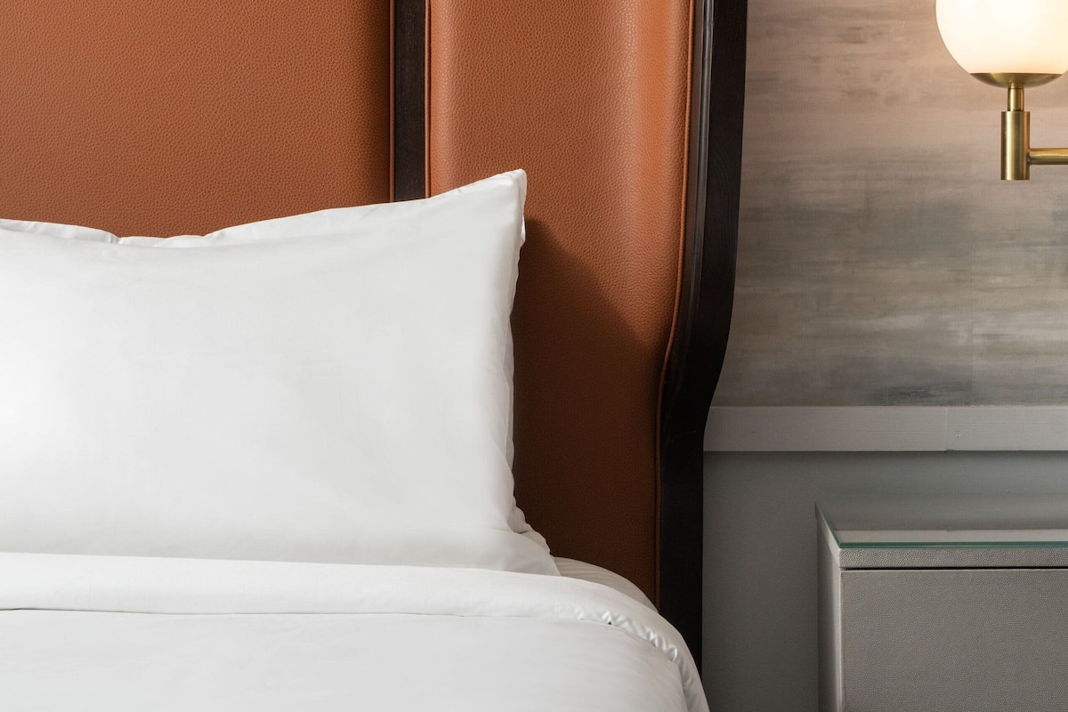 A bed with a brown headboard, a white pillow, and a bedside table with a lamp.