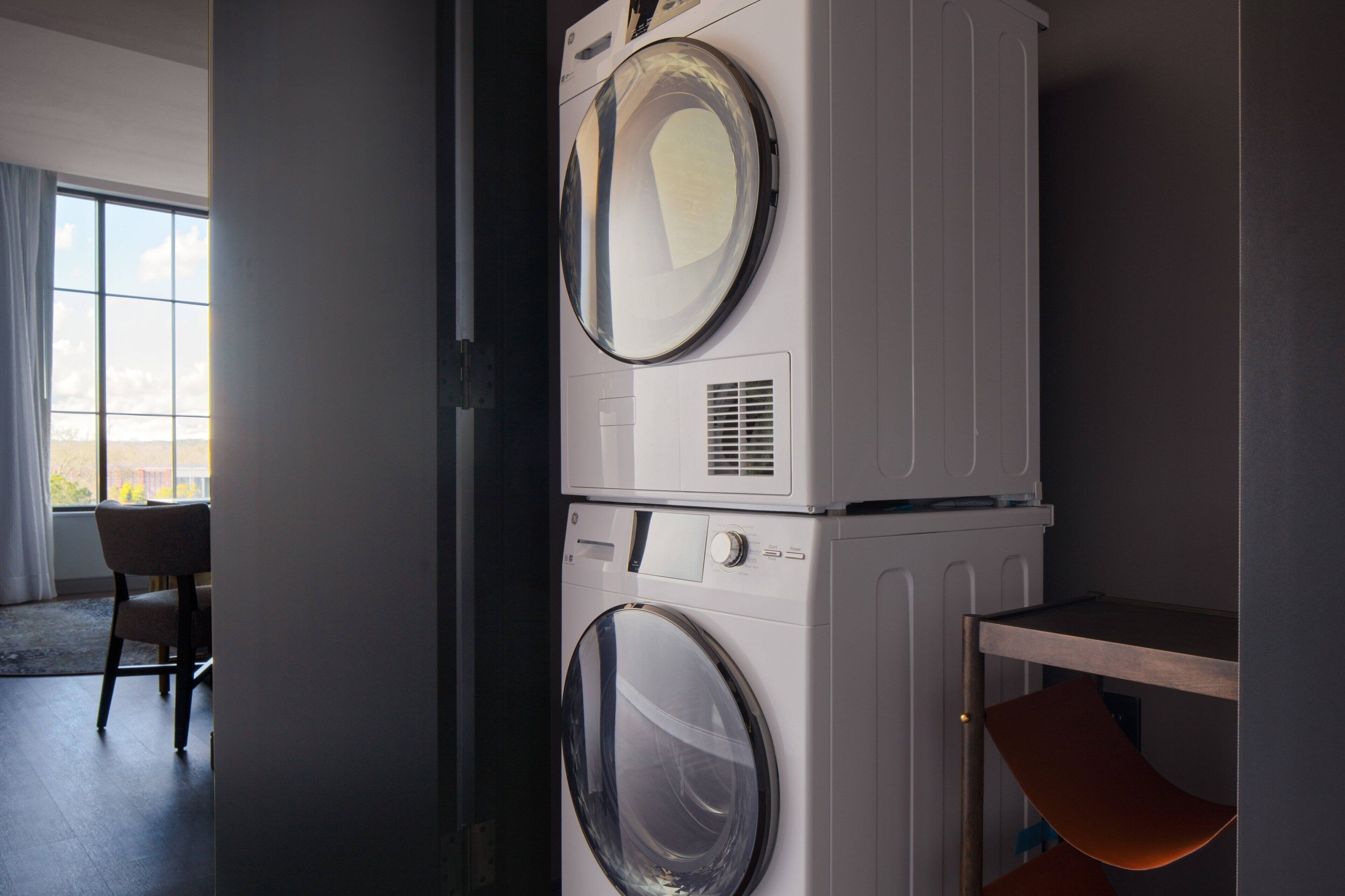 A laundry area with stacked washing machines and a chair.