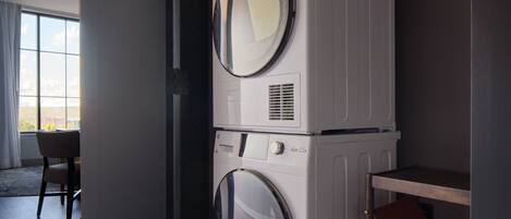 A laundry area with stacked washing machines and a chair.