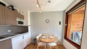 A compact kitchen with a dining area, a clock, and a window with a view.