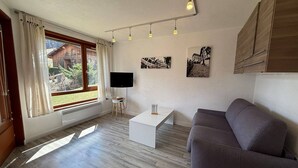 A modern living room with a grey sofa, a white coffee table, a flat-screen TV, and wooden flooring.